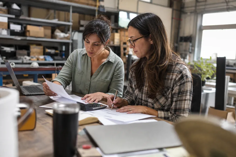 A business owner and a bookkeeper reviewing a card processing fee statement with a calculator