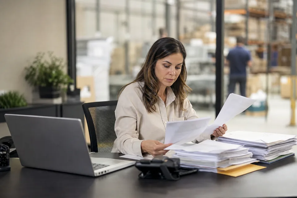 An accounts receivable manager reviewing customer invoices and remittance slips at her desk