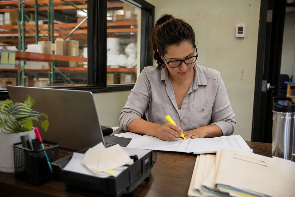 An AR manager at a small US distributor comparing two collections software proposals on her desk beside a laptop