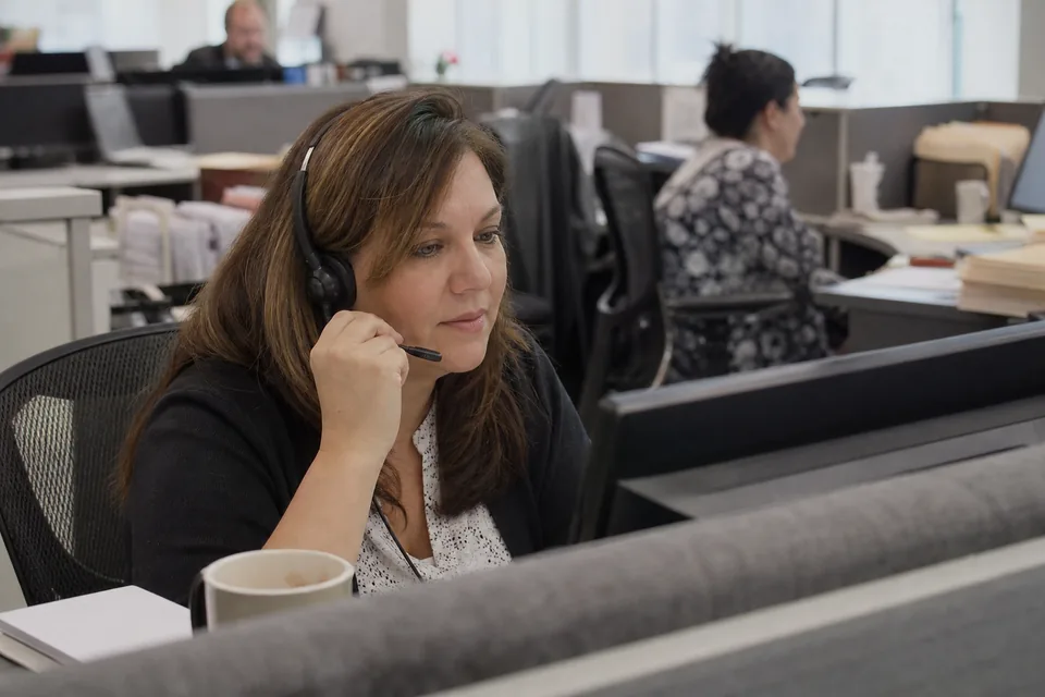 A collections specialist listening on a phone headset while reading a customer account on her monitor