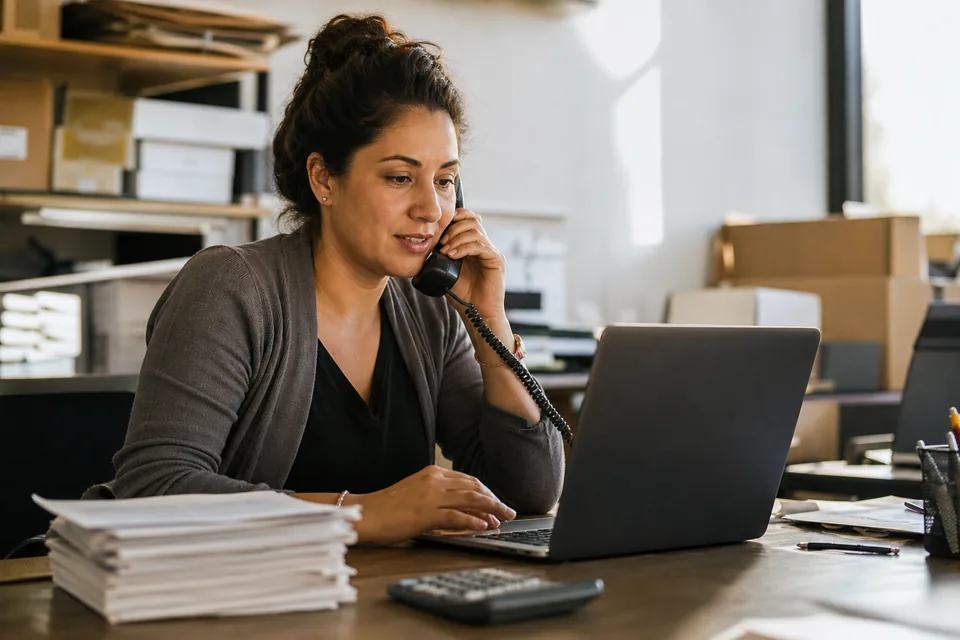 An AR specialist reading a customer reply on a laptop with paid invoice stubs on the desk