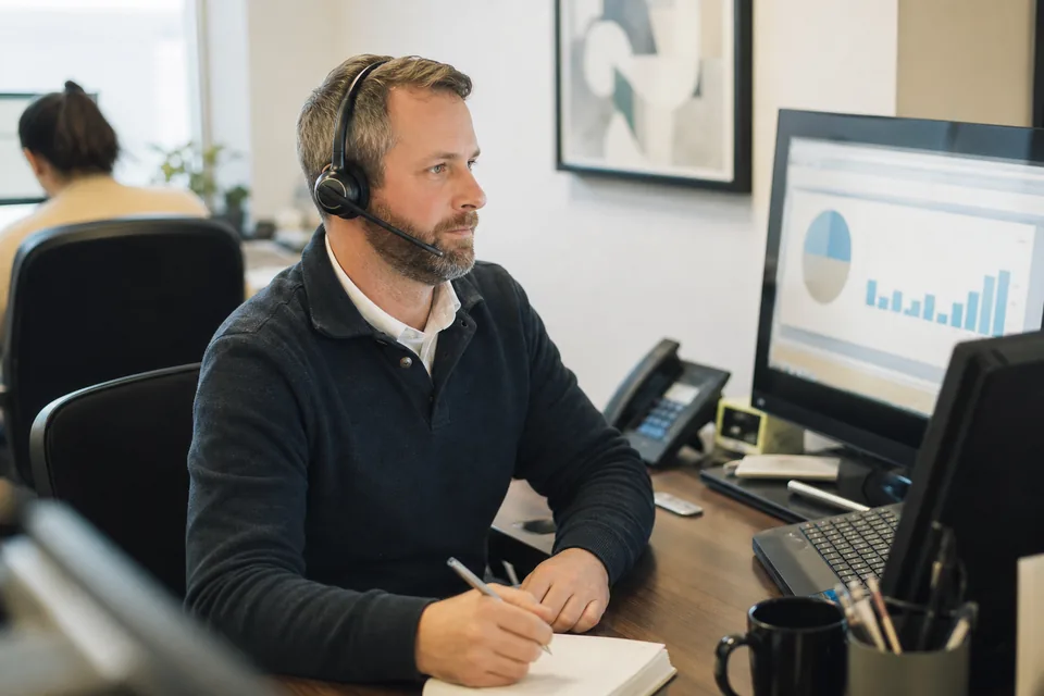 An AR specialist with a headset reviewing an aging report before a collections call